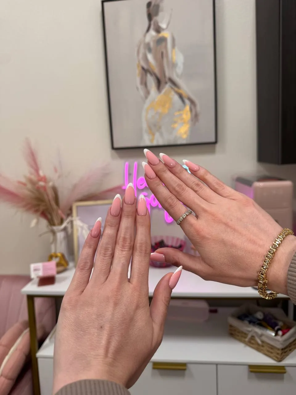 Long almond French manicures with white tips, in front of the studio's pink 'Hello Gorgeous' neon sign