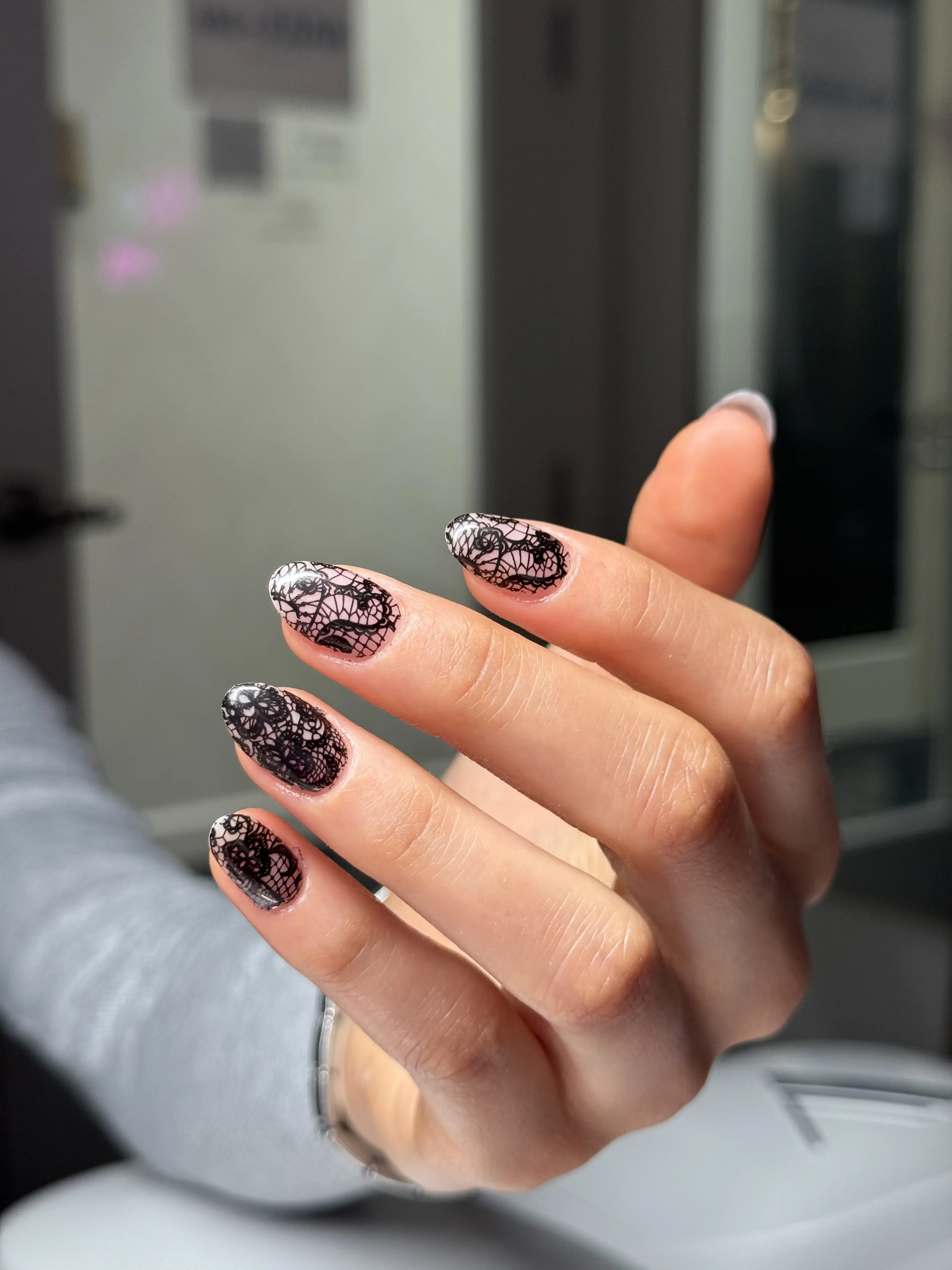Medium-length almond nails with a black lace pattern over a sheer nude base