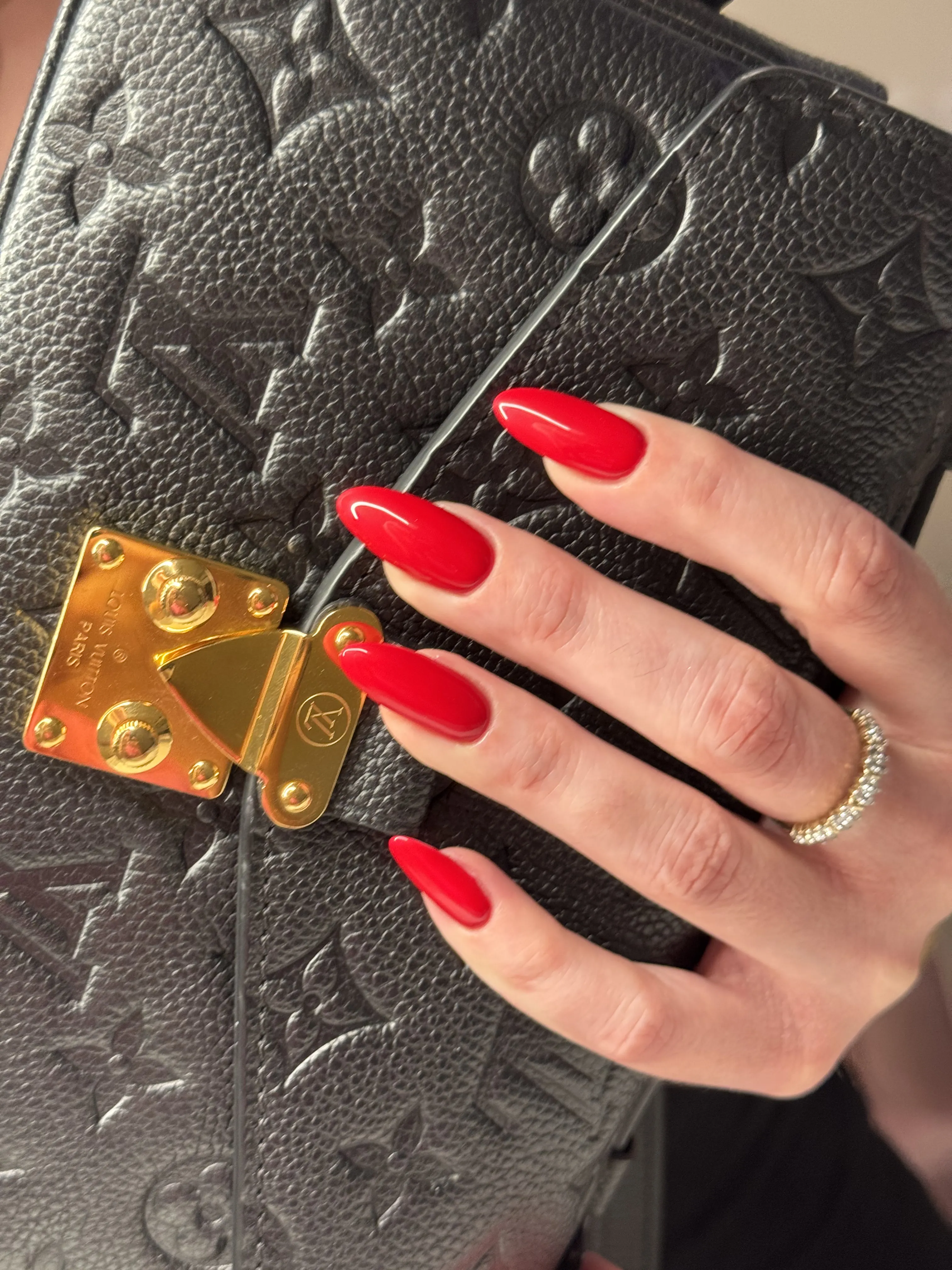 Long almond nails in glossy red gel polish on a black Louis Vuitton bag